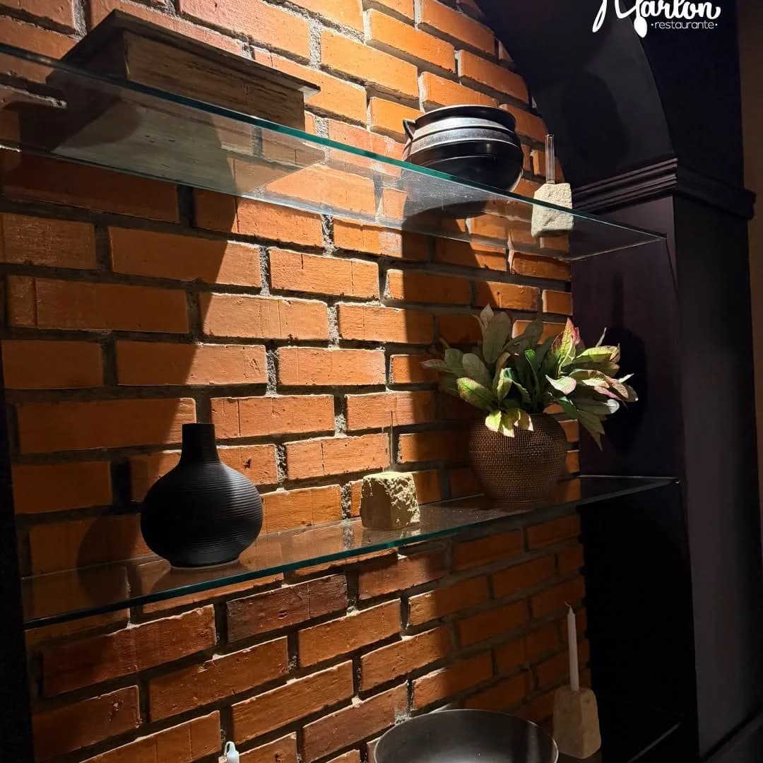Pared de ladrillo del salón de Marlon Restaurante con repisas y plantas.