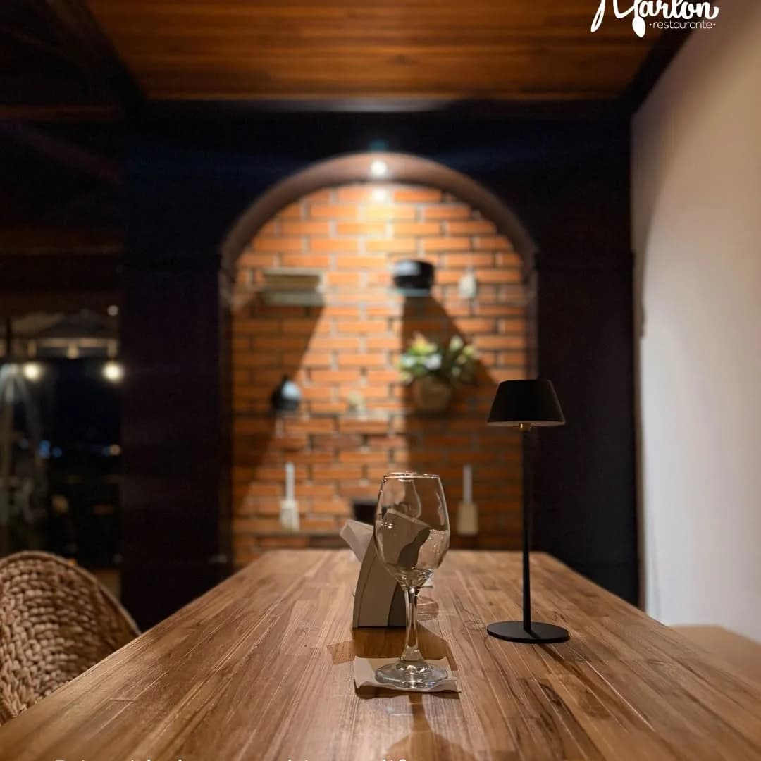 Rincón del salón de Marlon Restaurante, con mesa de madera, copa y pared de ladrillo.